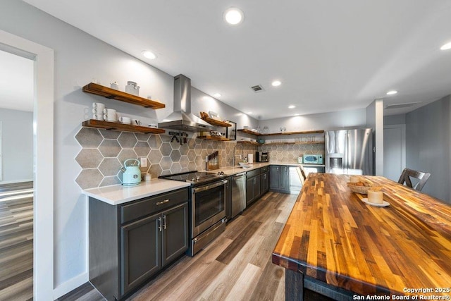 kitchen with sink, tasteful backsplash, island range hood, appliances with stainless steel finishes, and light hardwood / wood-style floors