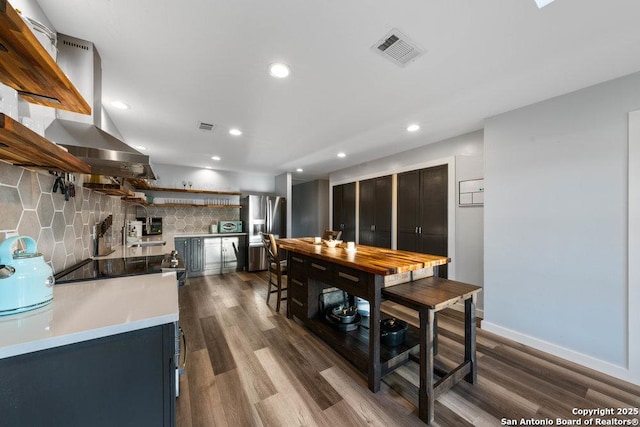 kitchen featuring sink, stainless steel refrigerator with ice dispenser, tasteful backsplash, island range hood, and dark hardwood / wood-style flooring