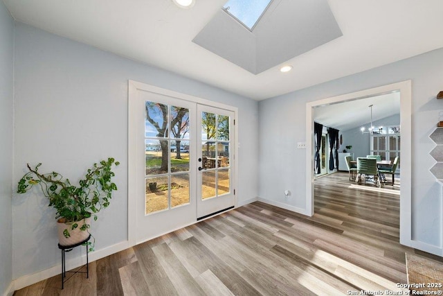 unfurnished room featuring vaulted ceiling with skylight, hardwood / wood-style floors, a chandelier, and french doors