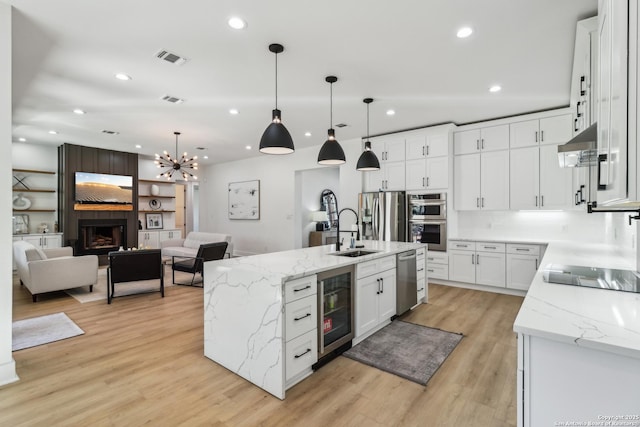 kitchen with wine cooler, open floor plan, stainless steel appliances, under cabinet range hood, and a sink