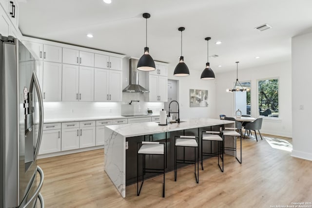 kitchen with stainless steel fridge, white cabinets, decorative backsplash, wall chimney exhaust hood, and a sink