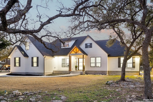 modern farmhouse style home featuring a shingled roof, a front yard, and stucco siding