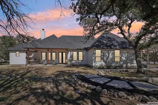 back of property at dusk featuring a chimney and a patio