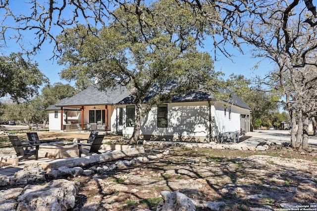 back of property featuring an attached garage, concrete driveway, an outdoor fire pit, and a patio area