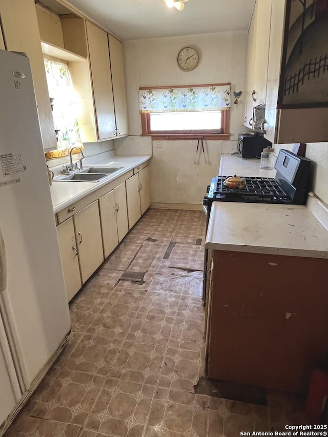 kitchen with sink, cream cabinets, white fridge, and stainless steel range with gas stovetop