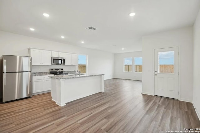 kitchen featuring appliances with stainless steel finishes, white cabinetry, an island with sink, sink, and light stone counters