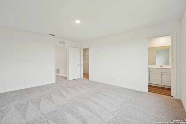 unfurnished bedroom featuring ensuite bath, a walk in closet, light colored carpet, and a closet