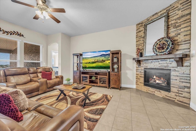 tiled living room featuring ceiling fan, a stone fireplace, and a textured ceiling