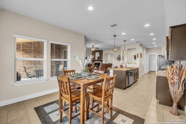 tiled dining area with a brick fireplace, sink, and ceiling fan