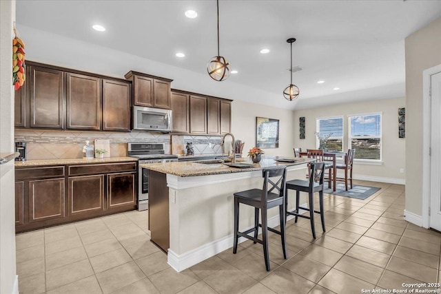 kitchen with pendant lighting, sink, light stone counters, stainless steel appliances, and a center island with sink