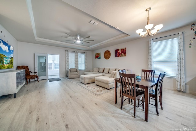 dining area featuring a raised ceiling, ceiling fan with notable chandelier, and light hardwood / wood-style flooring