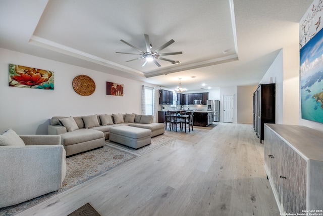 living room featuring a tray ceiling, ceiling fan with notable chandelier, and light wood-type flooring