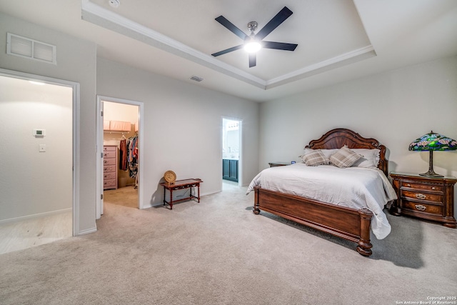 bedroom with ceiling fan, a tray ceiling, a walk in closet, light colored carpet, and a closet