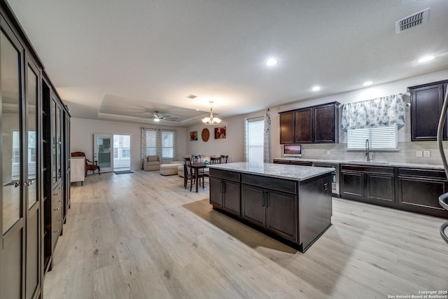 kitchen featuring a kitchen island, decorative light fixtures, sink, decorative backsplash, and a tray ceiling