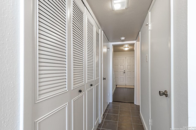 corridor featuring a textured ceiling and dark tile patterned floors