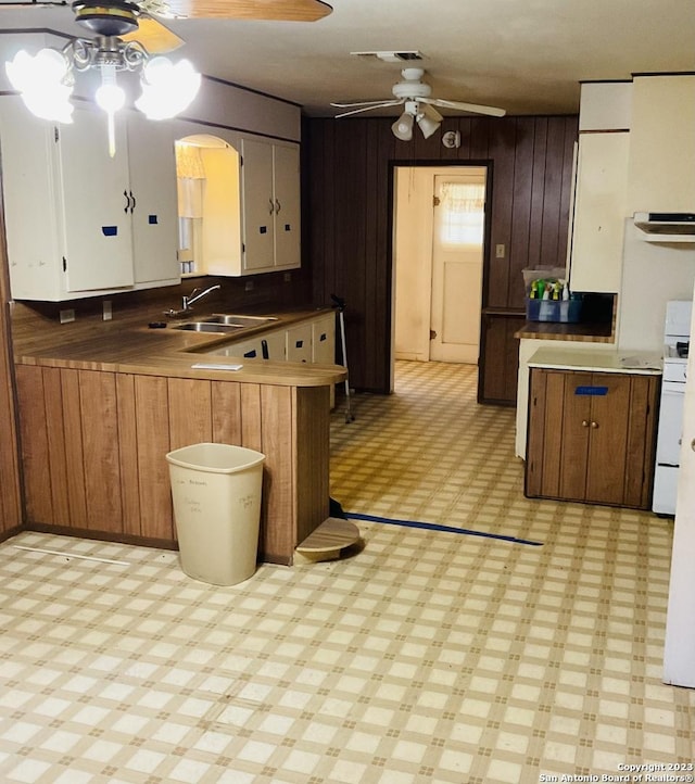 kitchen featuring sink, ceiling fan, stove, wooden walls, and kitchen peninsula