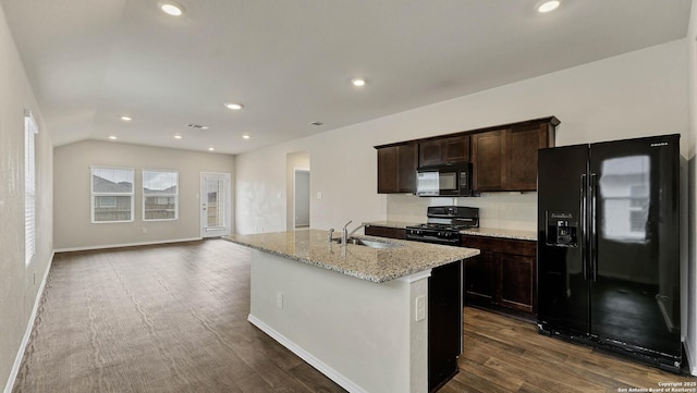 kitchen with sink, light stone counters, black appliances, an island with sink, and dark hardwood / wood-style flooring