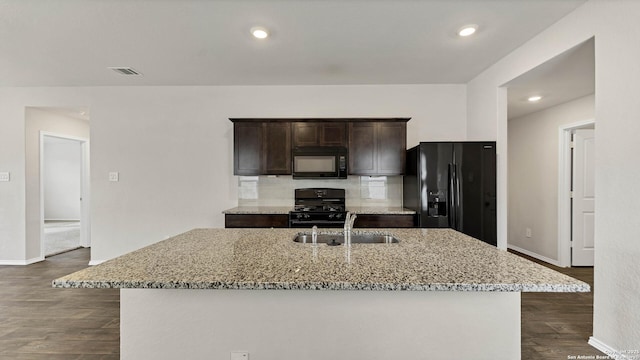 kitchen with sink, dark brown cabinets, black appliances, an island with sink, and light stone countertops