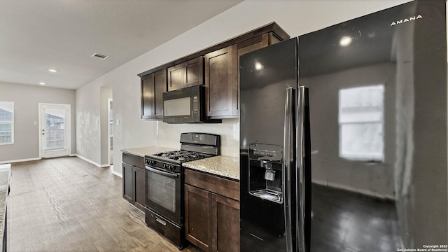 kitchen featuring light stone counters, dark brown cabinets, black appliances, and light hardwood / wood-style flooring