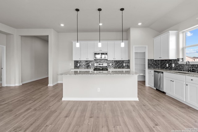 kitchen with appliances with stainless steel finishes, sink, white cabinets, hanging light fixtures, and a center island