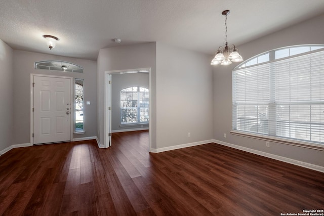 foyer entrance with dark wood-type flooring, a textured ceiling, and a chandelier