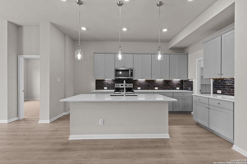 kitchen with appliances with stainless steel finishes, an island with sink, and hanging light fixtures