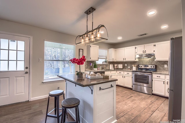 kitchen featuring a kitchen bar, white cabinetry, a center island, appliances with stainless steel finishes, and pendant lighting