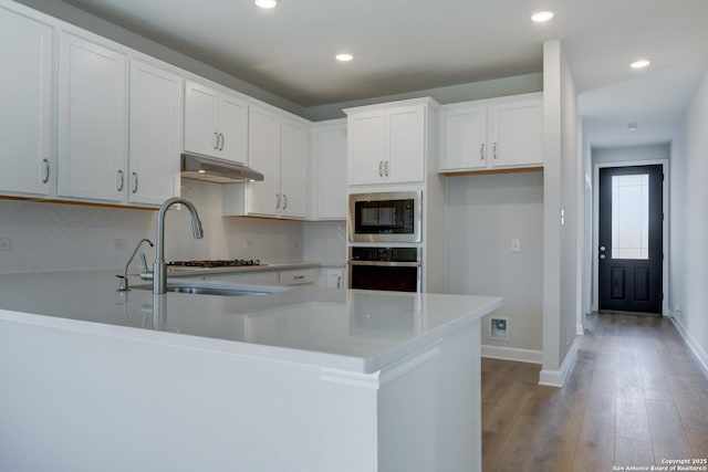 kitchen featuring built in microwave, white cabinets, oven, decorative backsplash, and light hardwood / wood-style flooring