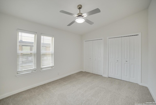 unfurnished bedroom with multiple closets, ceiling fan, lofted ceiling, and light carpet