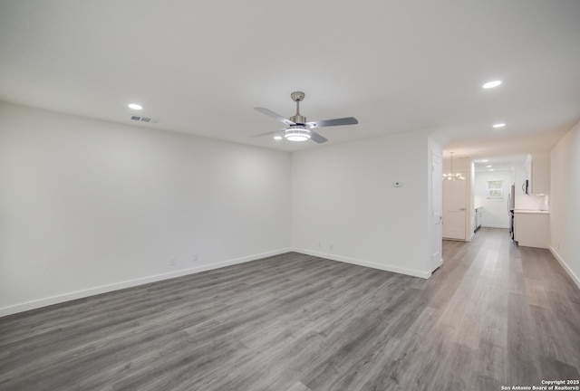 empty room featuring wood-type flooring and ceiling fan with notable chandelier