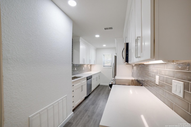 kitchen with hardwood / wood-style flooring, stainless steel appliances, decorative backsplash, and white cabinets