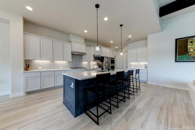 kitchen with stainless steel microwave, pendant lighting, white cabinetry, sink, and a kitchen island with sink