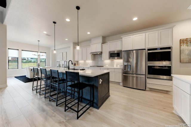 kitchen featuring pendant lighting, white cabinetry, a kitchen island with sink, stainless steel appliances, and tasteful backsplash