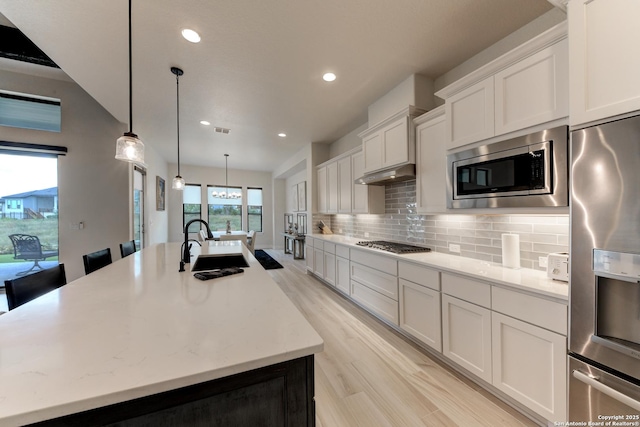 kitchen with sink, white cabinetry, a center island with sink, appliances with stainless steel finishes, and pendant lighting