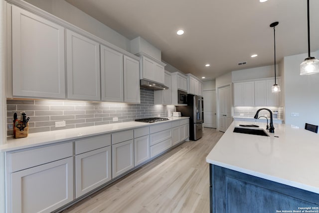 kitchen with sink, tasteful backsplash, decorative light fixtures, light hardwood / wood-style flooring, and stainless steel appliances