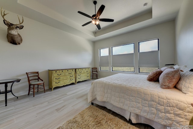 bedroom featuring a raised ceiling, ceiling fan, and light wood-type flooring