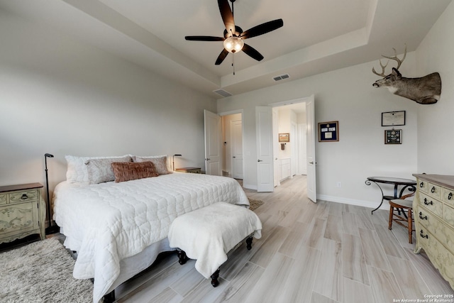 bedroom featuring light hardwood / wood-style flooring, a raised ceiling, and ceiling fan