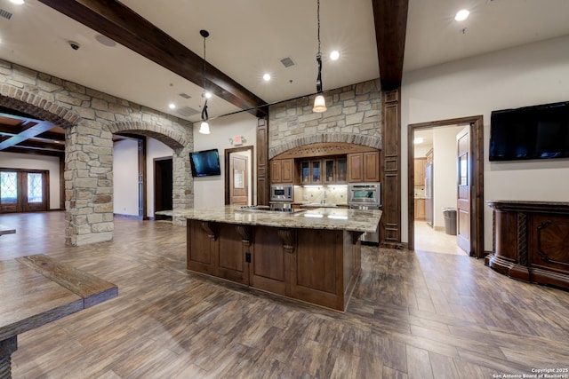 kitchen with a spacious island, a breakfast bar area, light stone counters, stainless steel microwave, and pendant lighting