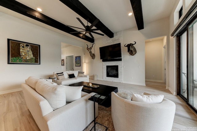 living room with beamed ceiling, a large fireplace, ceiling fan, and light hardwood / wood-style floors