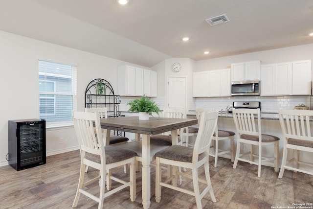 dining space with a healthy amount of sunlight, beverage cooler, vaulted ceiling, and light wood-type flooring