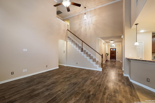 unfurnished living room with a high ceiling, dark hardwood / wood-style flooring, ornamental molding, and ceiling fan