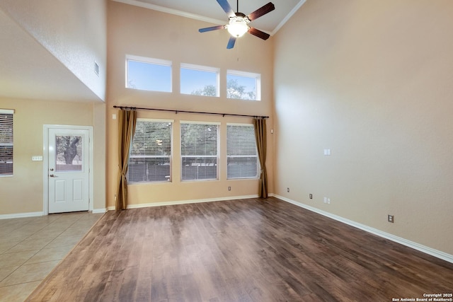 unfurnished living room with crown molding, a towering ceiling, ceiling fan, and light hardwood / wood-style floors