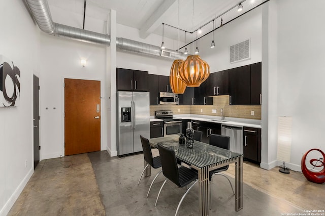 kitchen with pendant lighting, sink, stainless steel appliances, a high ceiling, and decorative backsplash