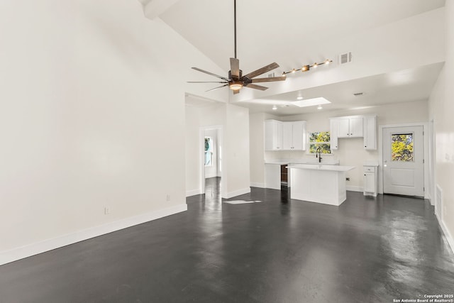 unfurnished living room featuring ceiling fan, high vaulted ceiling, a skylight, and sink