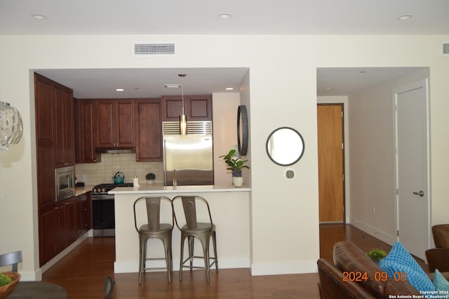 kitchen featuring a kitchen bar, built in appliances, kitchen peninsula, pendant lighting, and backsplash