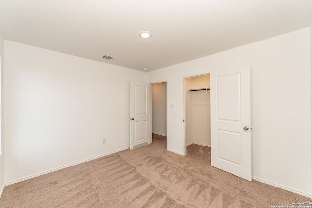 unfurnished bedroom featuring a walk in closet, light colored carpet, and a closet