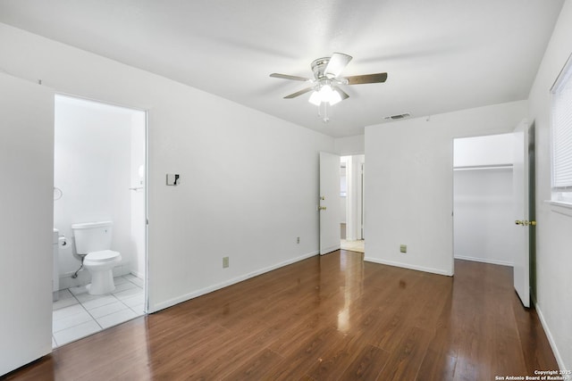 unfurnished bedroom with connected bathroom, a spacious closet, a closet, hardwood / wood-style flooring, and ceiling fan