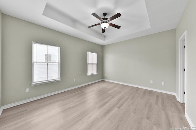 empty room featuring ceiling fan, a raised ceiling, and light wood-type flooring