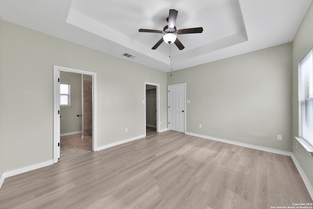 unfurnished bedroom featuring multiple windows, connected bathroom, a raised ceiling, and ceiling fan