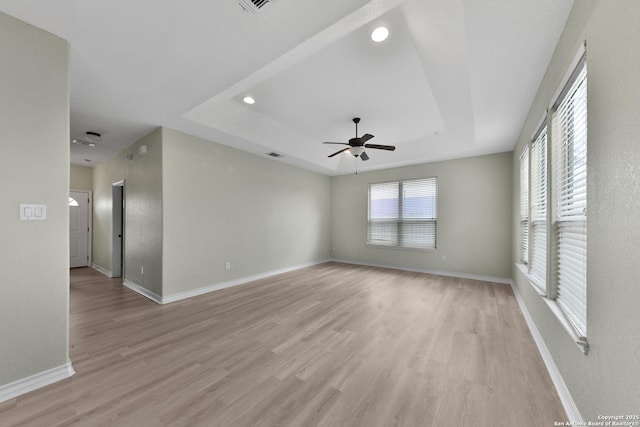 empty room featuring ceiling fan, a tray ceiling, and light hardwood / wood-style flooring